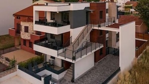 Un immeuble résidentiel moderne à plusieurs étages, doté d’un toit plat, de balcons et d’un escalier reliant les différents niveaux.