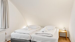 Una habitación pequeña y limpia con una cama, una mesita de noche con lámpara y una ventana con cortinas.