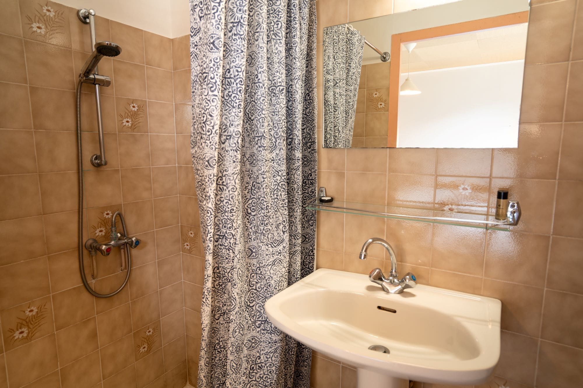 Un baño con ducha, lavamanos, repisa de vidrio y espejo.