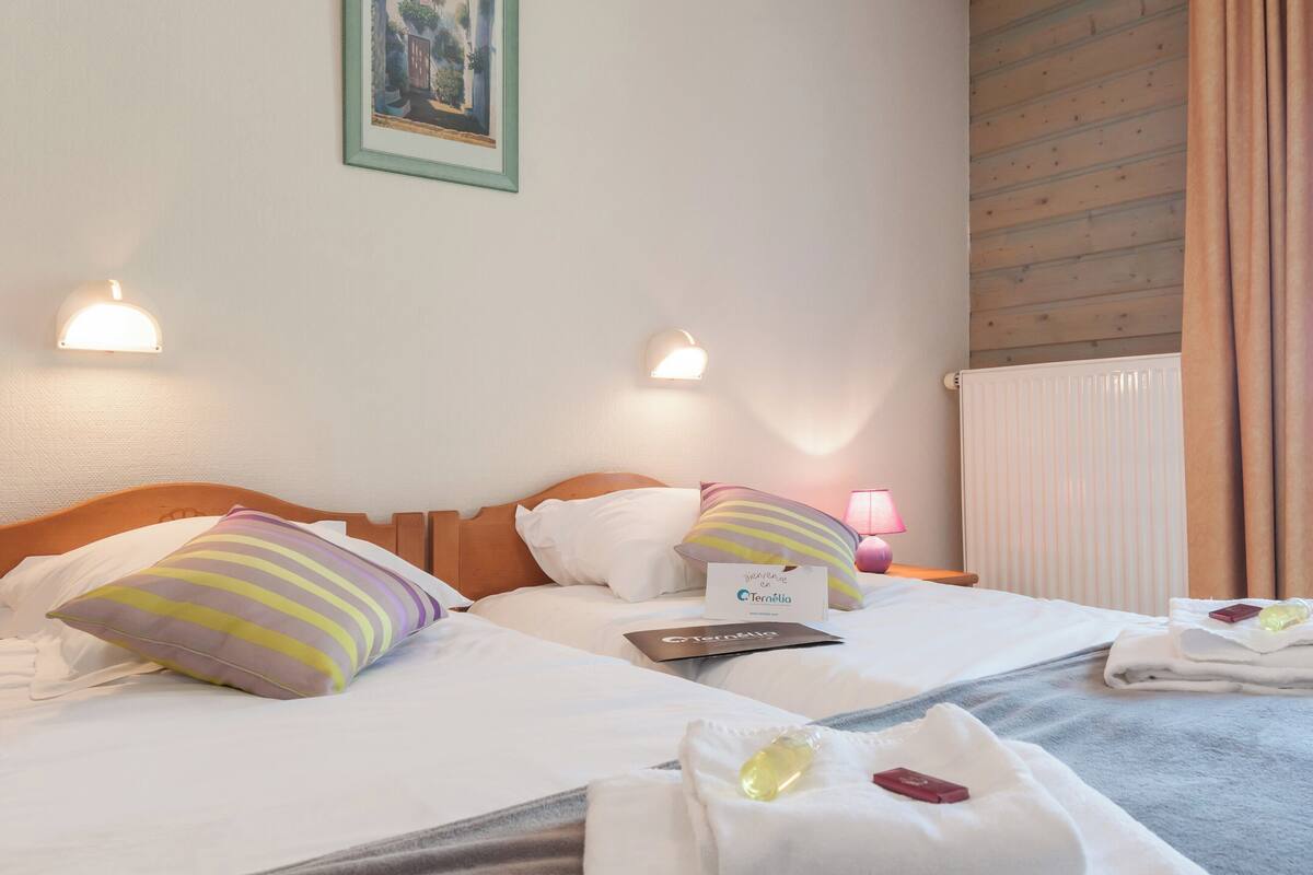 A hotel room with two beds, each with striped pillows, a bedside table with a lamp, and a framed picture on the wall.