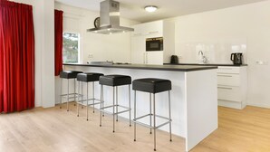 A modern kitchen with a central island, bar stools, a microwave, and a coffee maker. - Holiday Home in Midlaren, sauna (Midlaren)