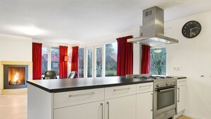 A modern kitchen with white cabinets, a stainless steel range hood, a built-in oven, and a large window with red curtains. - Holiday Home in Midlaren, sauna (Midlaren)