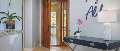 Un pasillo con una puerta de madera, un escritorio con lámpara y una pared con un letrero decorativo.