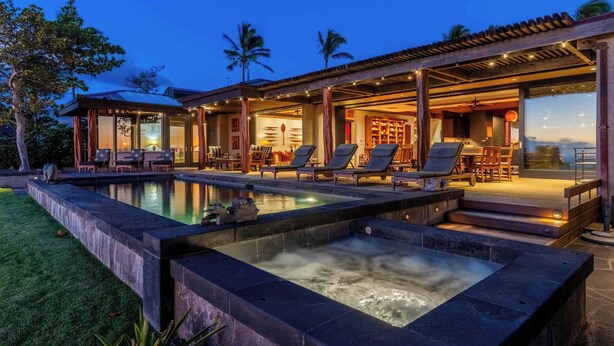 Een luxe buitenzwembad met ligbedden en een jacuzzi, omringd door een overdekt terras en uitzicht op de oceaan.