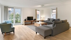Un salon moderne avec un canapé gris, un fauteuil bleu, une table basse en bois et un téléviseur posé sur un meuble en bois.