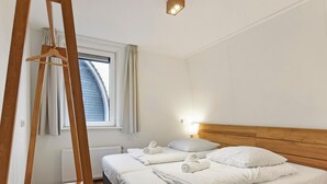 Une chambre d’hôtel avec deux lits, une échelle en bois, une fenêtre avec des rideaux et une lampe fixée au mur.