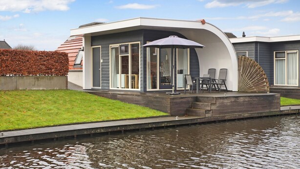Een modern huis met een overdekte buitenruimte, een klein terras en een kanaal ervoor.