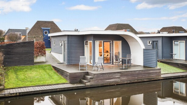 Ein modernes Haus mit einer Terrasse, einem kleinen Garten und einem Wasserbecken im Vordergrund.