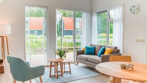 Ein modernes Wohnzimmer mit Sofa, Esstisch und Stuhl. Ein Fenster mit Jalousien, eine Uhr an der Wand und eine Pflanze auf dem Fensterbrett.