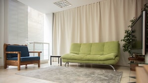 A living room with a green sofa, a blue chair, a small table, and a TV on a stand. - Spacious apartment nearby restaurants, cafes and 2 minutes walk from the metro!
 (Athens)