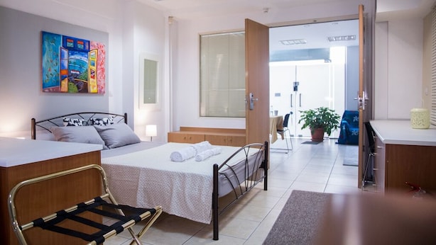 A hotel room with a bed, a desk, a chair, a window with blinds, and a painting on the wall. - Spacious apartment nearby restaurants, cafes and 2 minutes walk from the metro!
 (Athens)