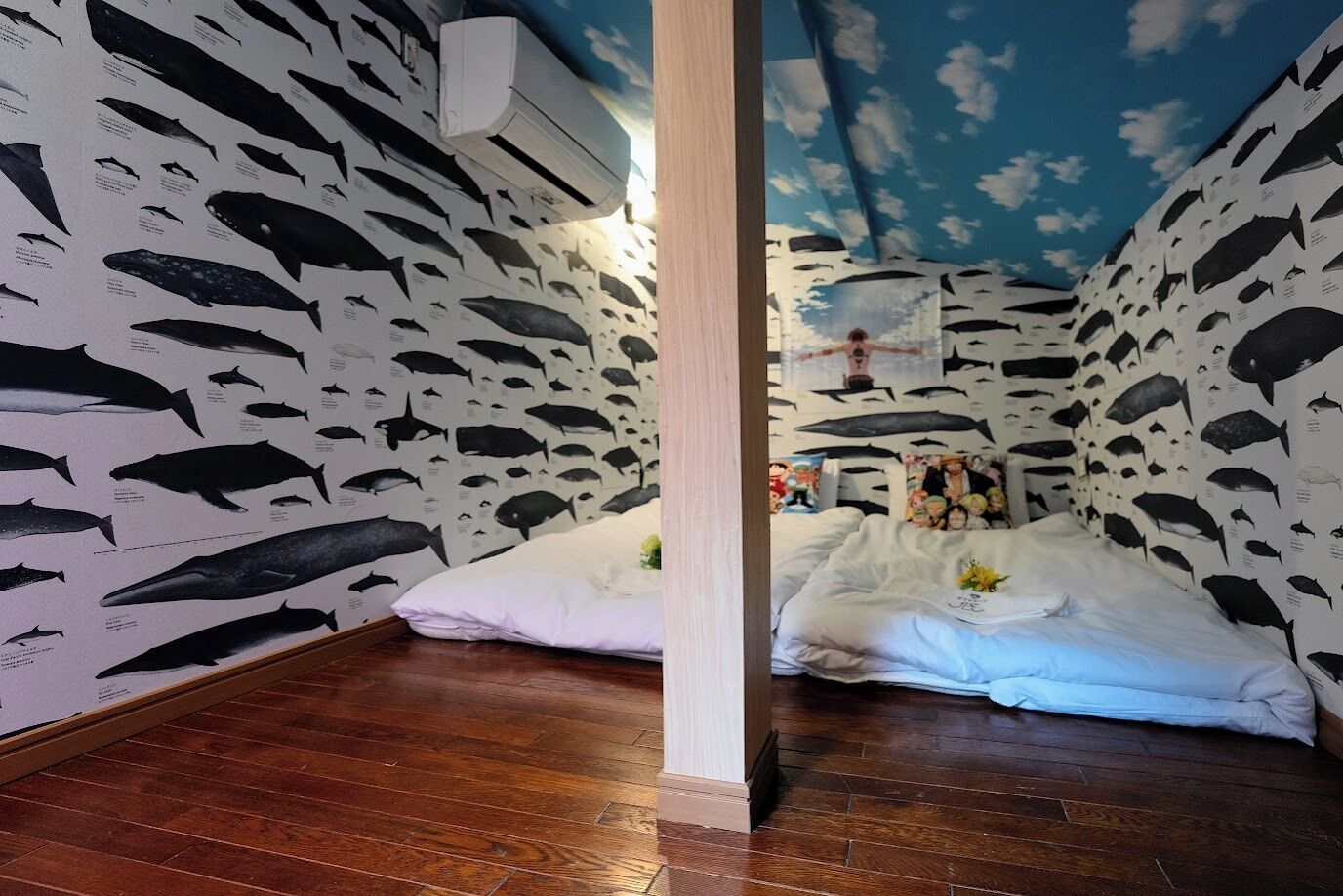 Une pièce dont les murs sont recouverts d’illustrations de poissons, avec un lit à la literie blanche et un plancher en bois.