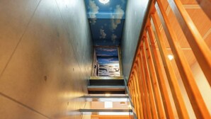 Una escalera con barandilla de madera que lleva a una habitación con cielo y nubes pintados en el techo.