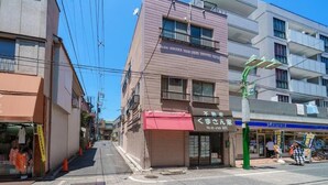 Vista de la calle con un edificio que tiene escaparates y un toldo rojo, con un letrero en japonés.