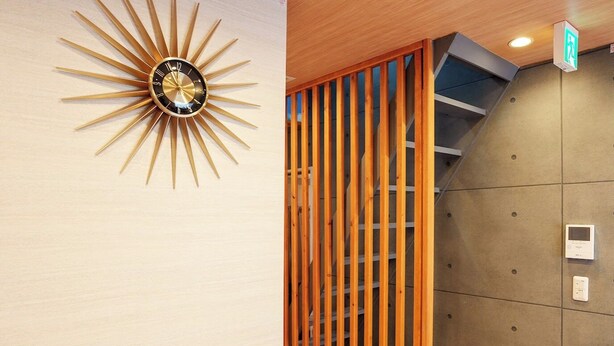 A sunburst wall clock, a wooden slat partition, and a control panel on a wall.