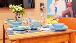 A dining table set with blue plates, glasses, and cutlery, with a floral centerpiece and a Pikachu-themed mural in the background.