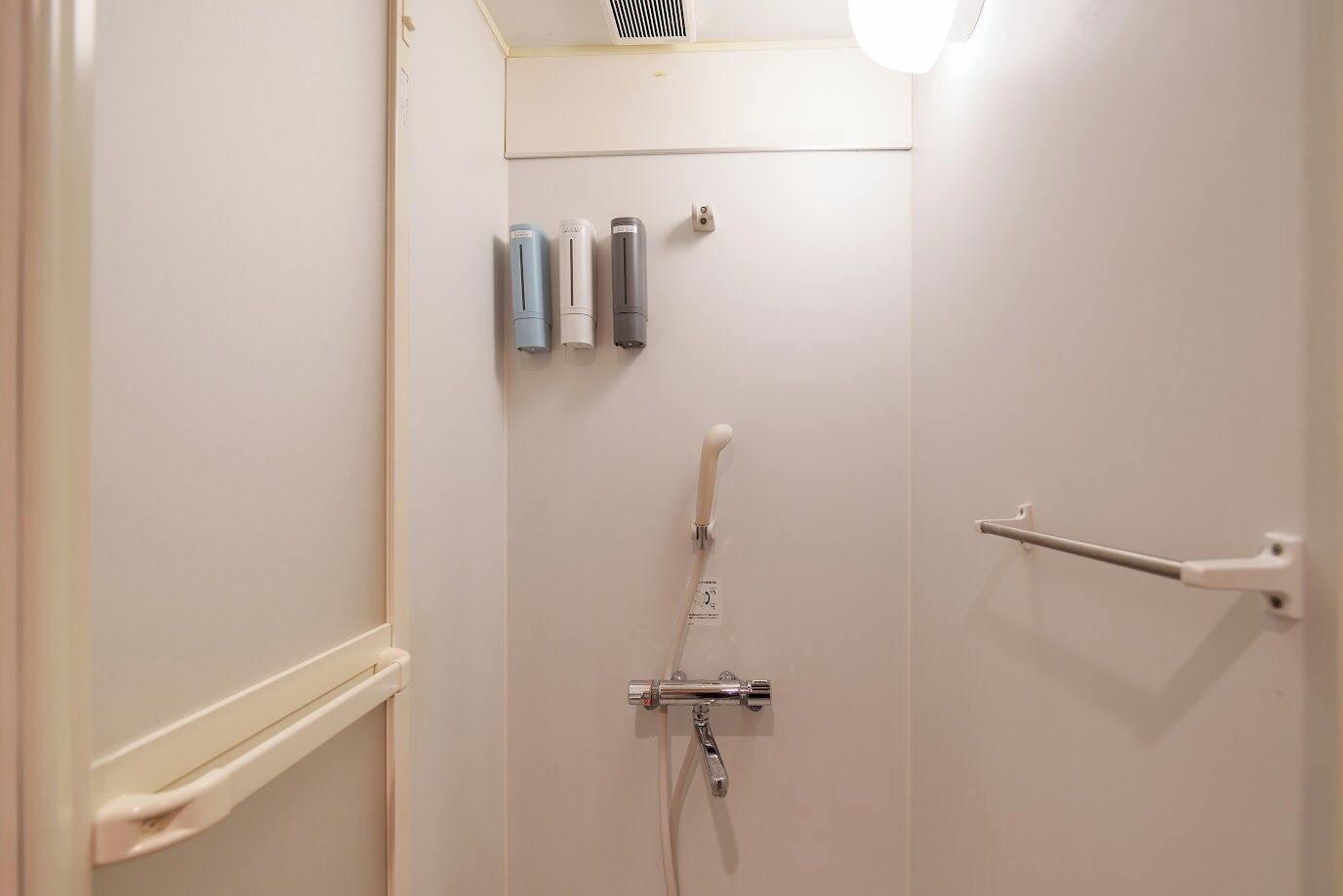 A bathroom with a shower, a towel rack, and a hand dryer.