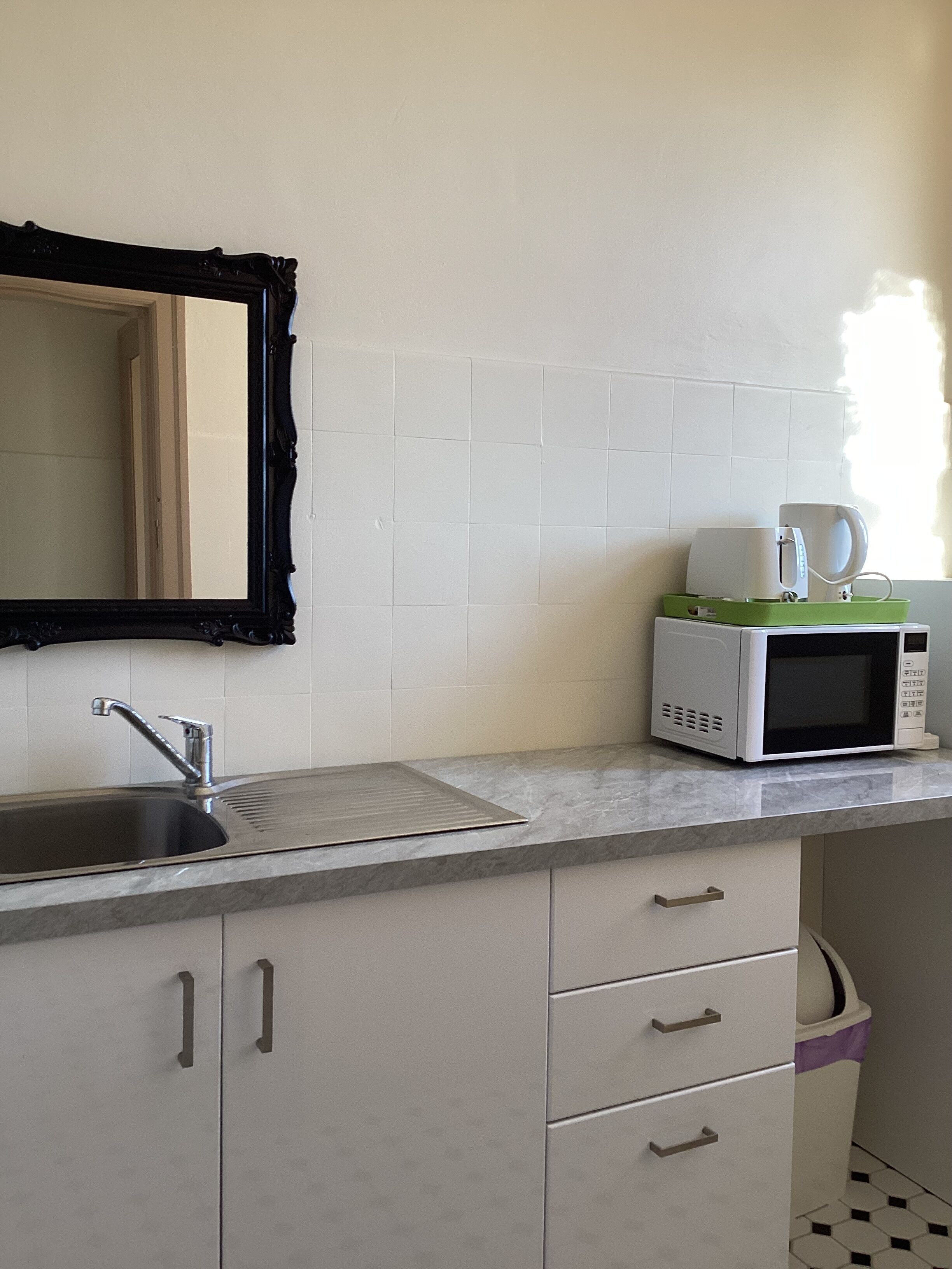Una cocina con un lavabo, microondas y cafetera sobre la encimera.