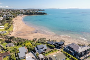 Une zone résidentielle côtière avec des maisons modernes, une plage de sable et une eau d’un bleu limpide.