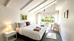 A bedroom with a bed, bedside table, lamp, and a window with a view of greenery.