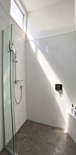 A modern bathroom with a glass shower enclosure, white tiled walls, and a built-in faucet. - Hidden Clifftop Gem
>Ocean Views
>Clifftop
>Walk to Beach
>Quiet Escape (Auckland)