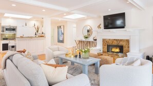 A modern living room with a fireplace, a television, and a kitchen in the background. - La Jolla Living by AvantStay | A+ Location | Private Backyard Lounge (San Diego)