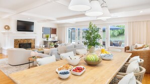 A spacious living room with a wooden dining table, sofas, and a large window offering a view of the outdoors. - La Jolla Living by AvantStay | A+ Location | Private Backyard Lounge (San Diego)