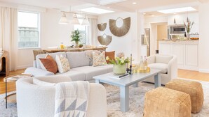 A modern living room with a sofa, ottomans, and a coffee table. There is a kitchen area with a dining table and chairs. - La Jolla Living by AvantStay | A+ Location | Private Backyard Lounge (San Diego)