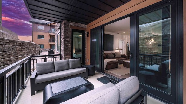 A modern outdoor living area with a stone wall, a sofa set, and a glass door leading to a room. - Frontgate 211 - 3 Bedroom Residence (Avon)