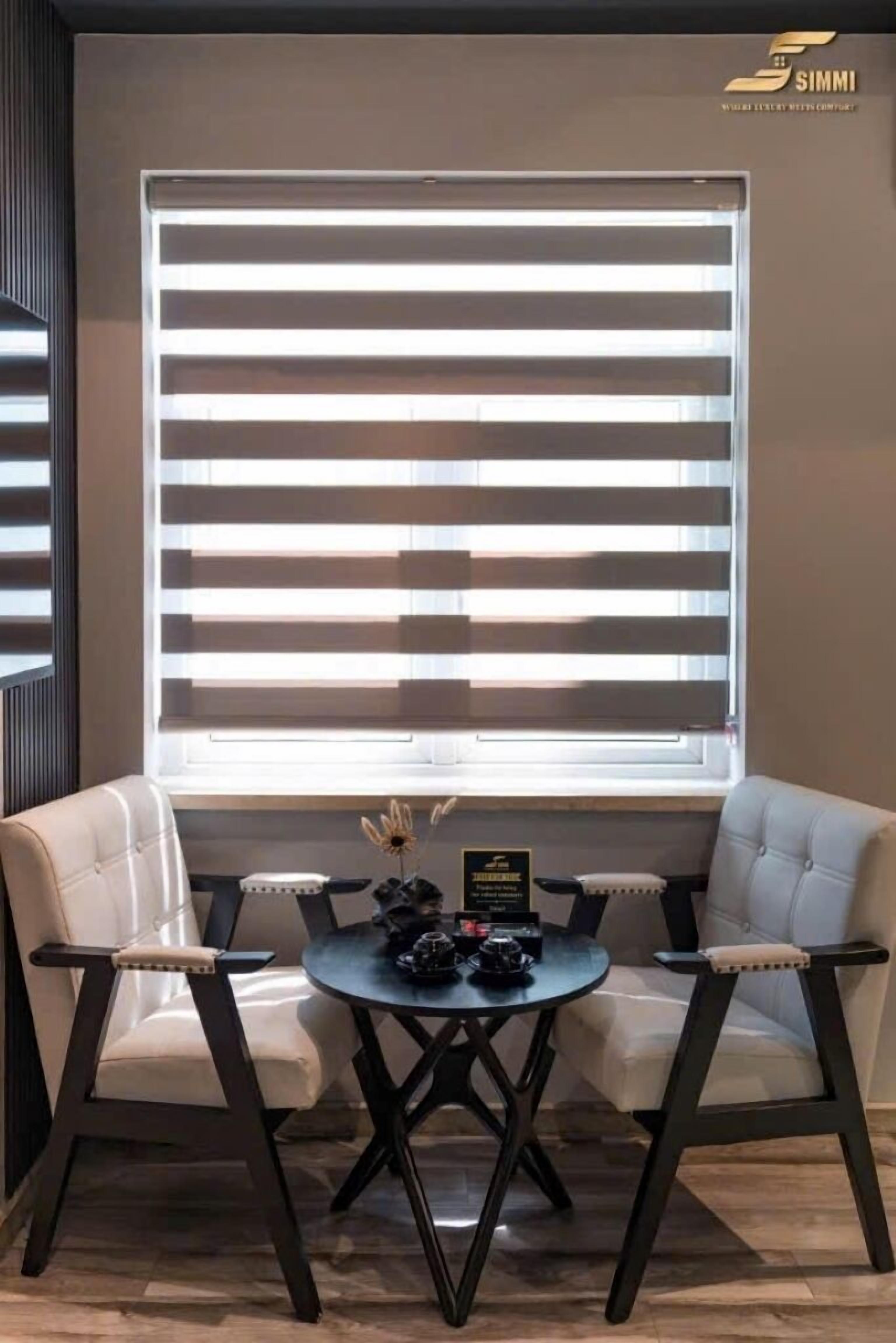 A modern room with a large window with horizontal blinds, two white leather sofas, a small round table with a vase and a book, and a black coffee table.