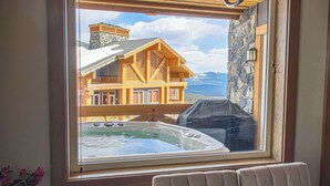 Een kamer met een groot raam met uitzicht op een houten chalet en een hottub.