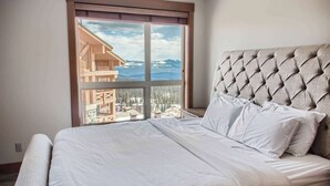 Hotelkamer met een bed, een groot raam met uitzicht op een berg en gebouwen, en een gestoffeerd hoofdeinde.