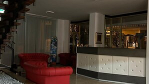A modern lobby with a staircase, red leather sofas, a reception desk, and a view of the outside. - Hotel Marea (Cattolica)