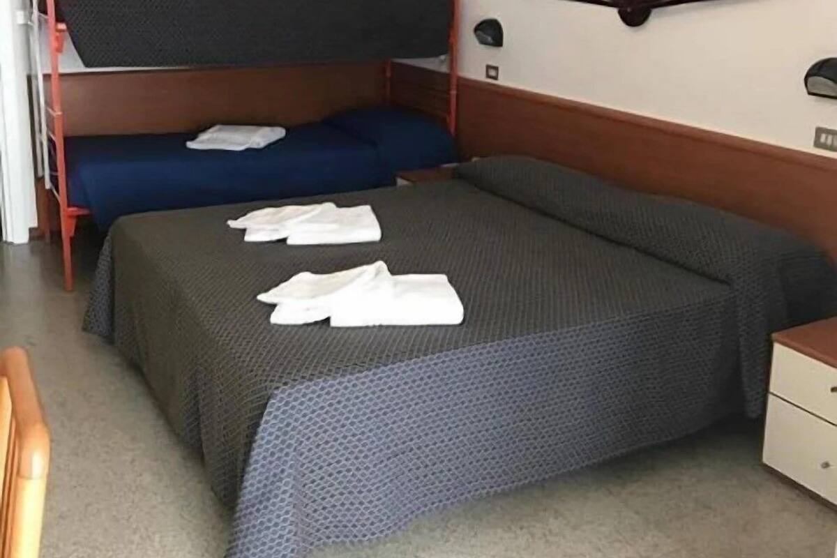 A double bed with a grey and blue bedspread, two white towels, and a wooden headboard.