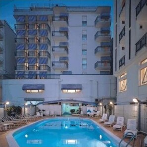 Un hotel con piscina, sillas de descanso y balcones.