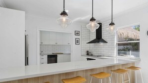 A modern kitchen with white cabinetry, a large island with bar stools, pendant lighting, and a view of the outdoors. - The Seabreeze Sanctuary (WOORIM)