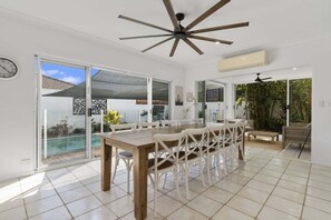 A spacious dining area with a wooden table and white chairs, a ceiling fan, and a sliding glass door leading to a pool. - The Seabreeze Sanctuary (WOORIM)
