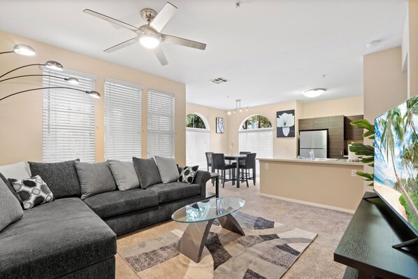A modern living room with a sectional sofa, a glass coffee table, and a ceiling fan.