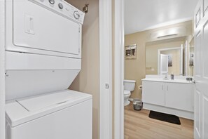 A laundry room with stacked washers and dryers, a toilet, and a vanity with a mirror.