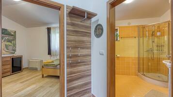 A modern bathroom with a glass shower enclosure, a wooden floor, and a bed with a green blanket.