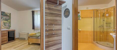 A modern bathroom with a glass shower enclosure, a wooden floor, and a bed with a green blanket.