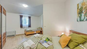 A bedroom with a bed, a bedside table, a mirror, a window with curtains, and a painting on the wall.