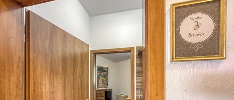 A wooden door leading to a room with a tiled floor, a framed certificate on the wall, and a small desk with a chair.