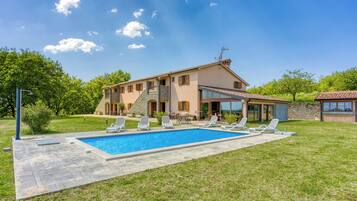 A two-story house with a swimming pool, outdoor seating, and a stone facade.