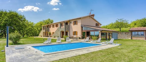 Une maison à deux étages dotée d’une piscine, d’un espace extérieur aménagé et d’une façade en pierre.
