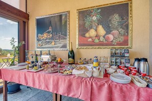 A breakfast buffet with various food items, a bottle of wine, and two paintings on the wall.