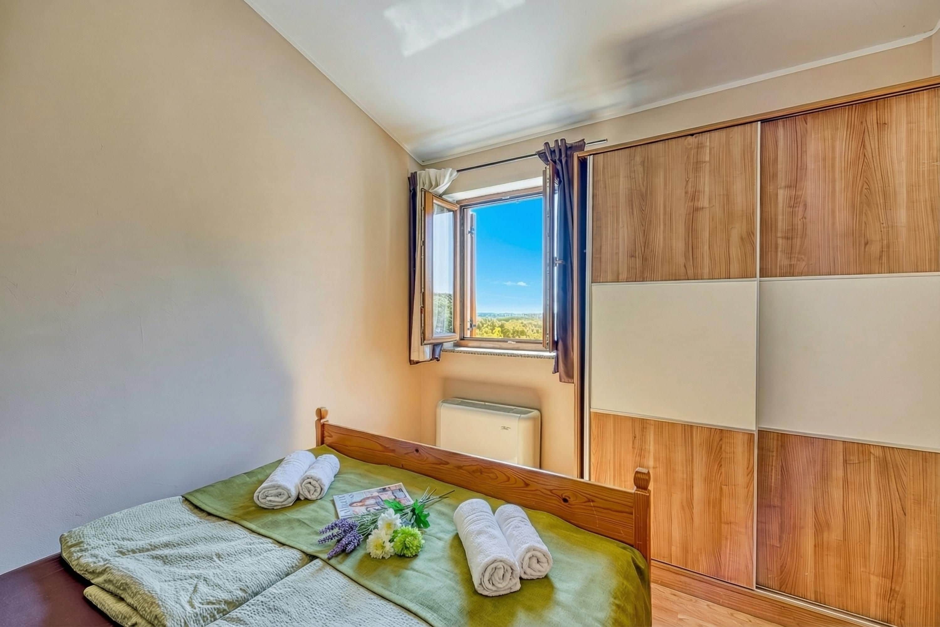 Un dormitorio con cama, ventana con cortinas, armario de madera y vistas al exterior.