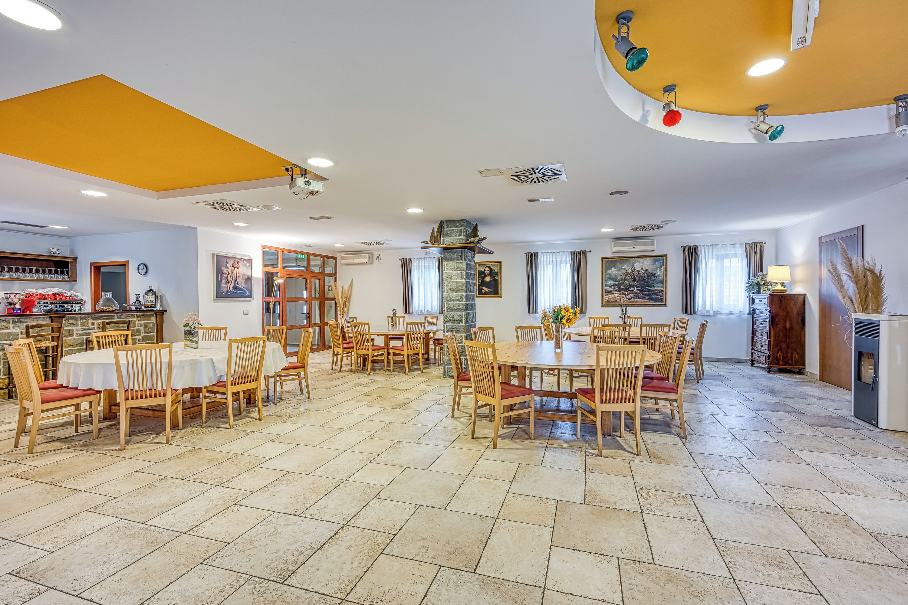 A spacious dining area with multiple tables and chairs, a stone fireplace, and a kitchen area with a bar.