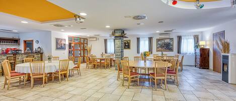 A spacious dining area with multiple tables and chairs, a stone fireplace, and a kitchen area with a bar.