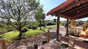A wooden deck with a pergola, potted plants, and a view of a grassy landscape.